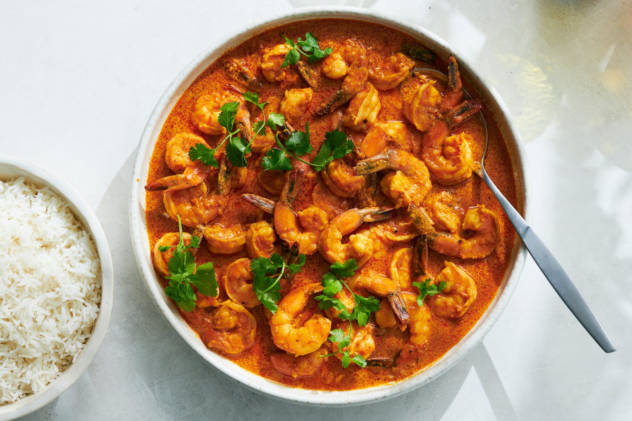 Shrimp topped with parsley sit in a red-orange curry. A spoon is sticking out of the bowl.