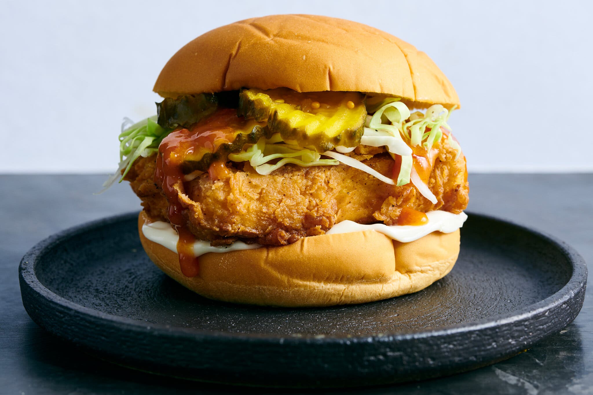 A side image of a sandwich piled high with a block of fried tofu, lettuce and pickles.