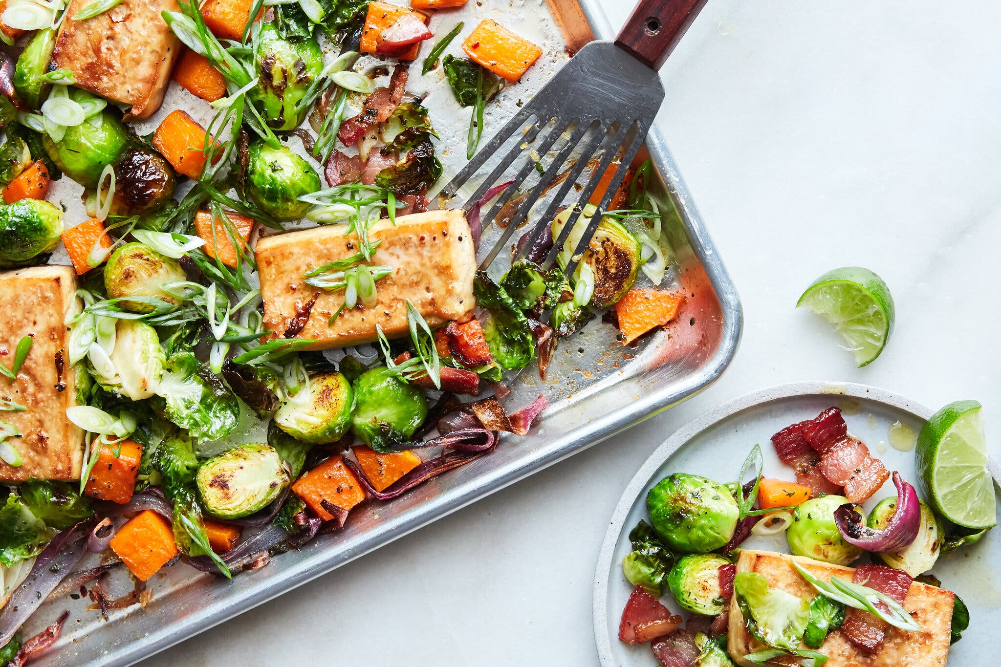 An overhead image of maple-roasted tofu on a pan surrounded by brussels sprouts and cubed sweet potato.