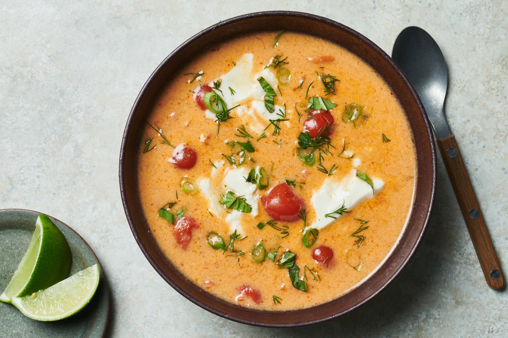 An overhead image of a bowl of orange broth spotted with blocks of tofu and tiny tomatoes.