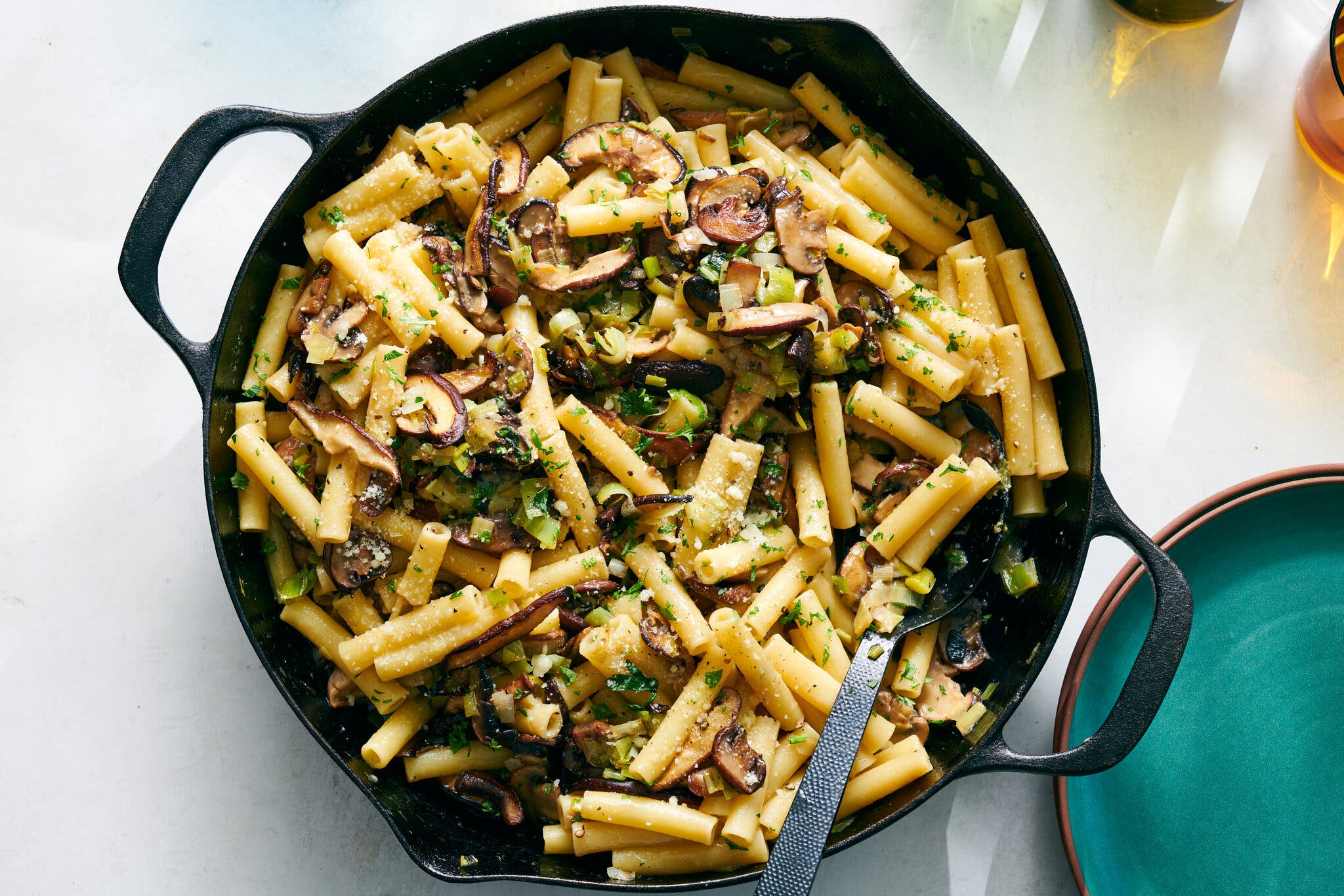 A skillet with two handles is filled with pasta topped with mushrooms and leeks.