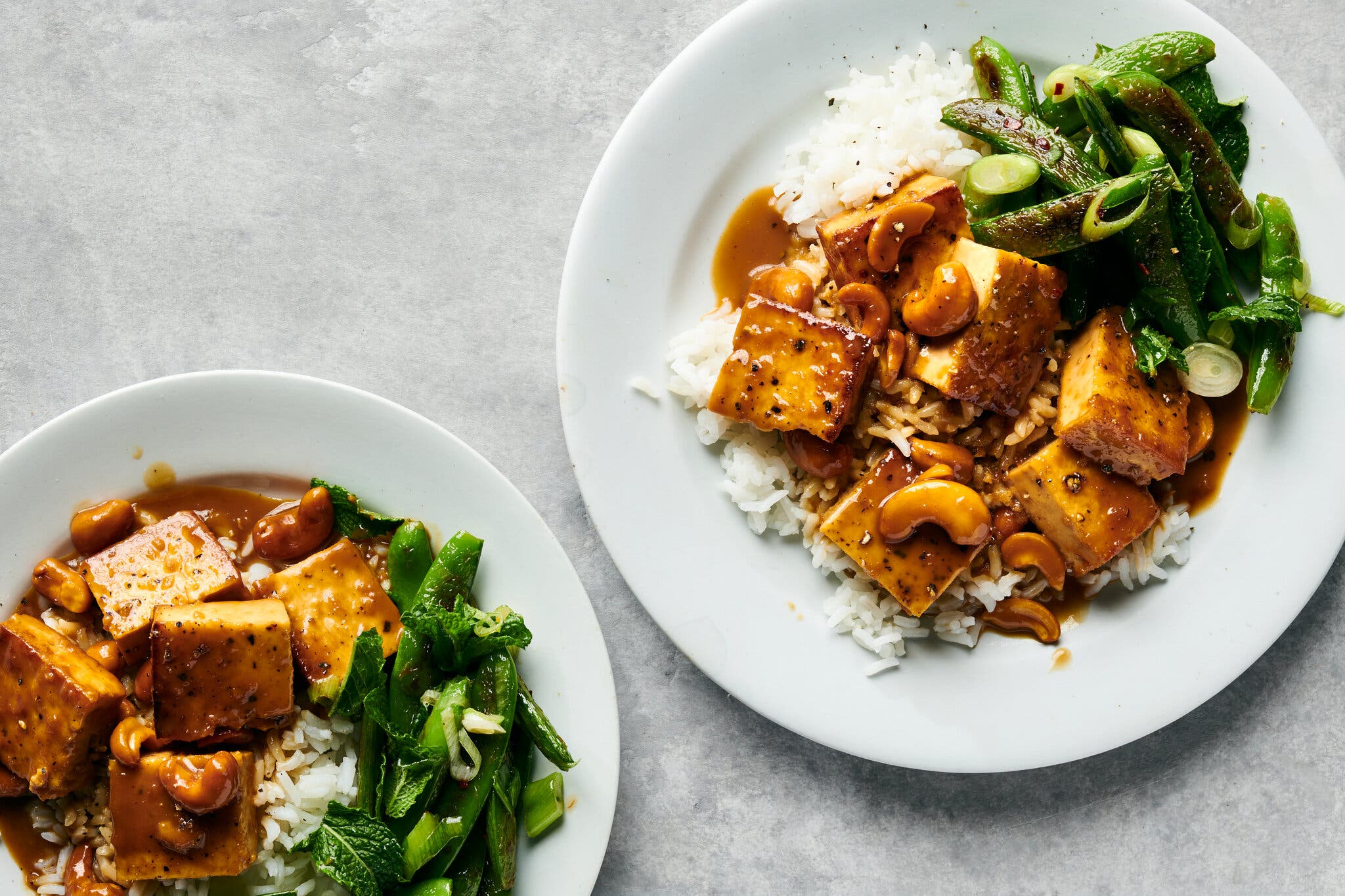 An overhead image of two plates topped with cubed, sauced tofu and snap peas.