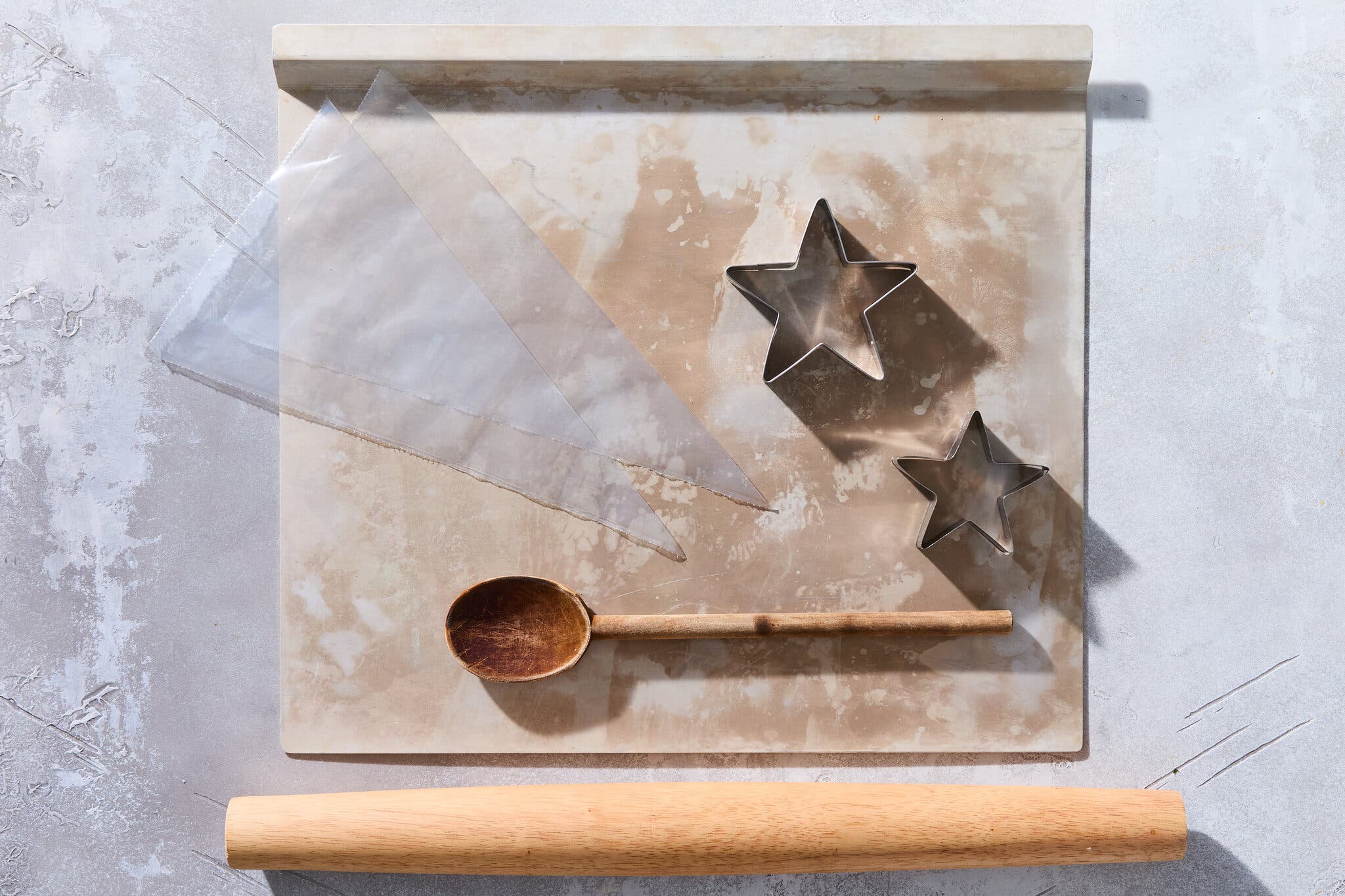 An overhead image of cookie baking tools including parchment paper, piping bags, cookie cutters, a wooden spoon and a rolling pin.