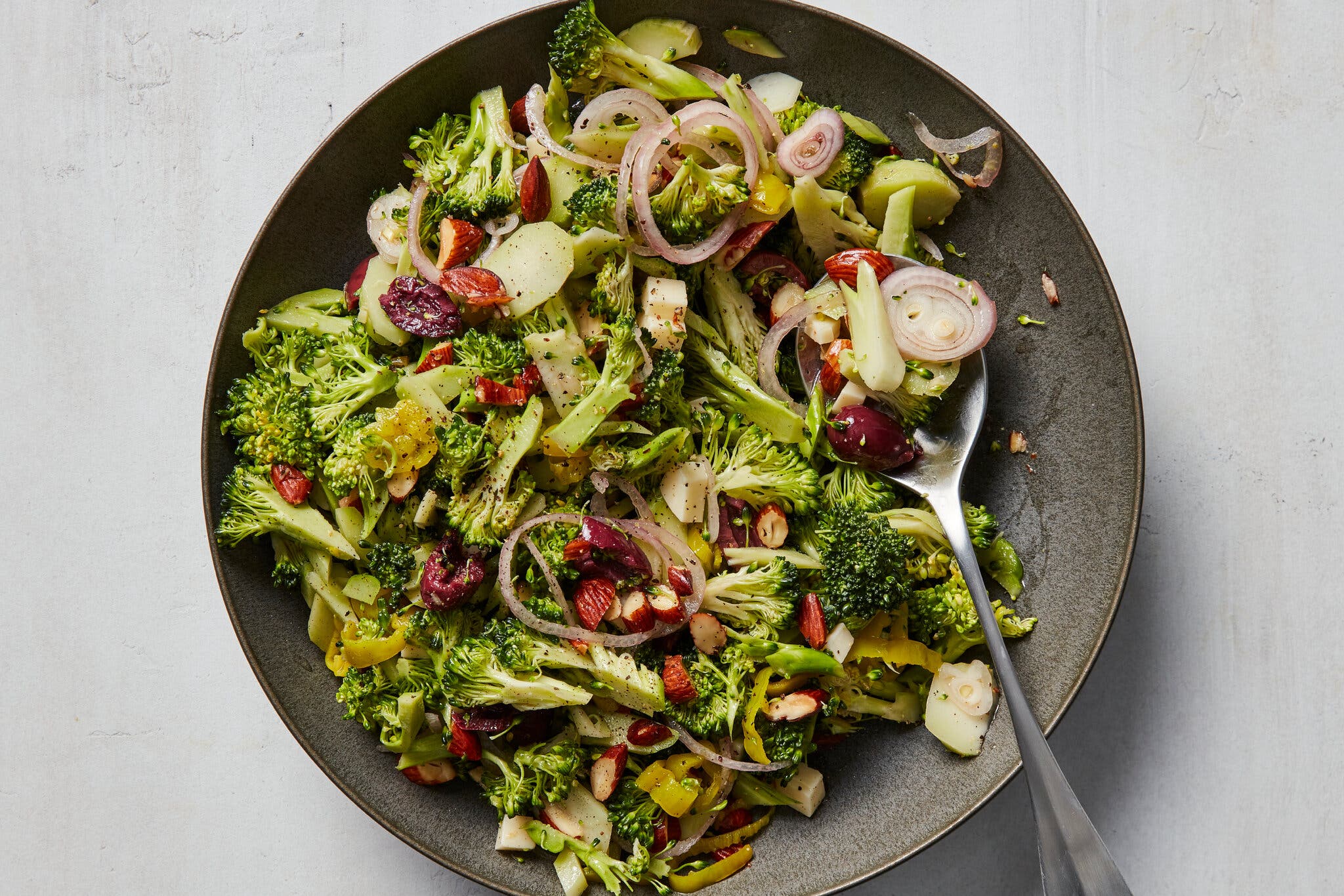 An overhead image of a black plate topped with broccoli, almonds, nuts and shallots.