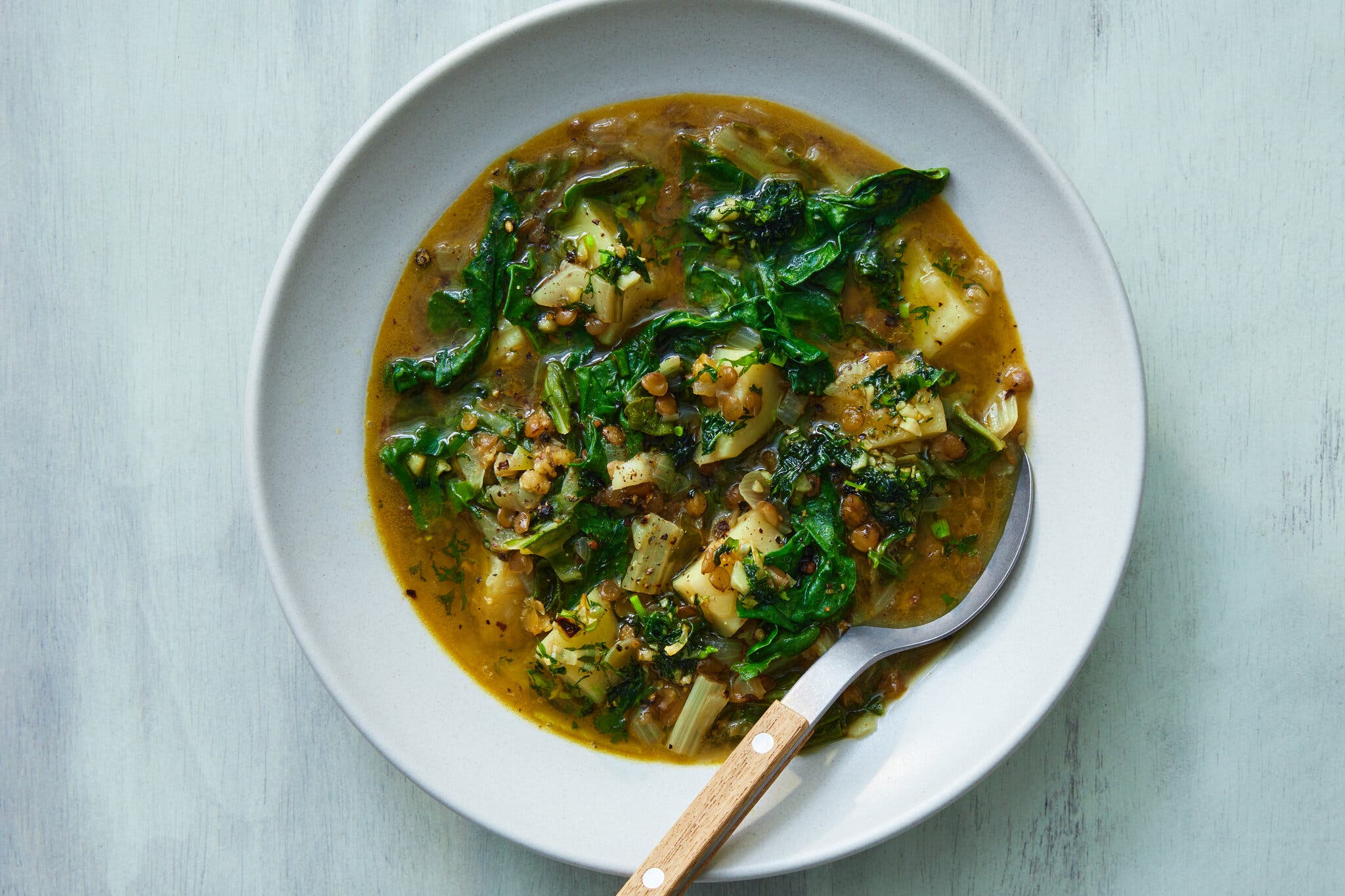 An overhead image of a lentil soup run through with greens.