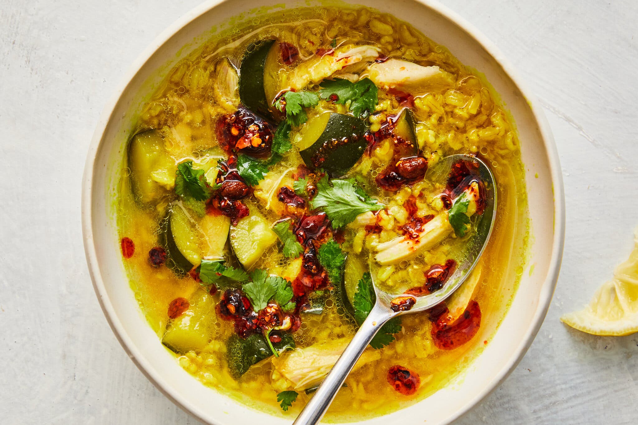 An overhead image of a bowl of soup filled with chicken and zucchini.