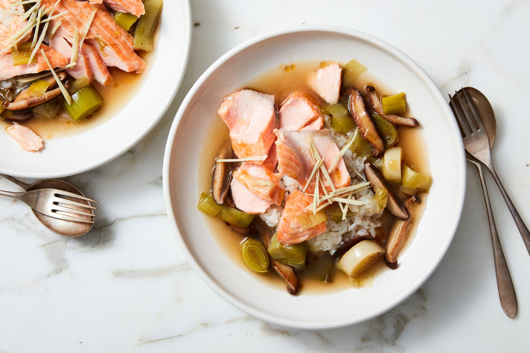 Poached salmon pieces served in a shallow bowl of broth with white rice, sliced shiitake mushrooms and leeks.