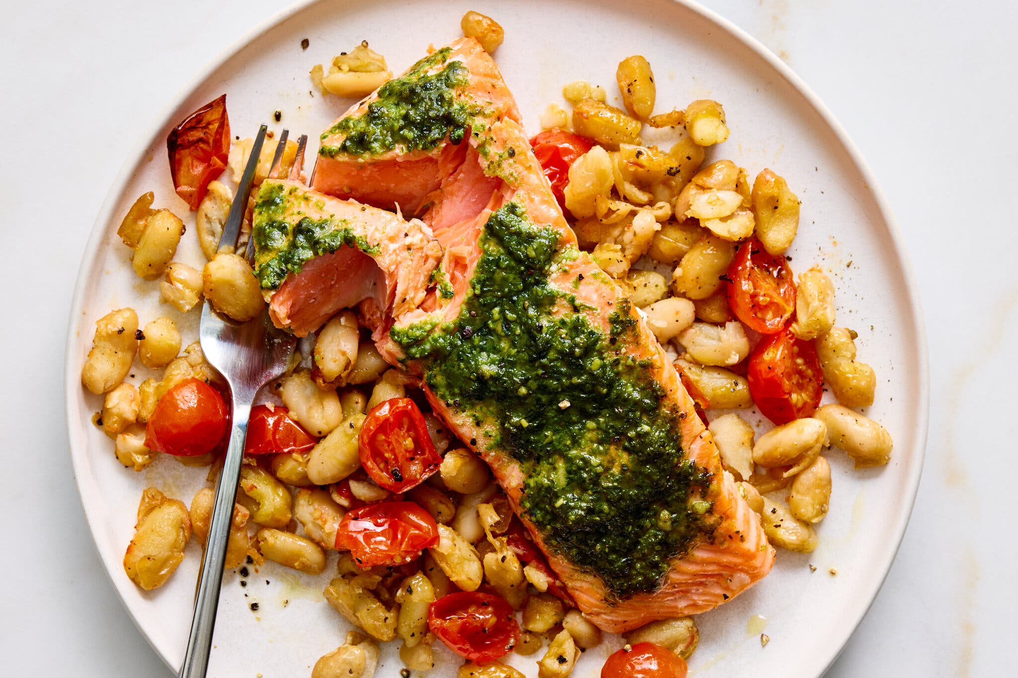 A seared salmon fillet topped with bright green pesto, served over a bed of white beans and roasted cherry tomatoes.