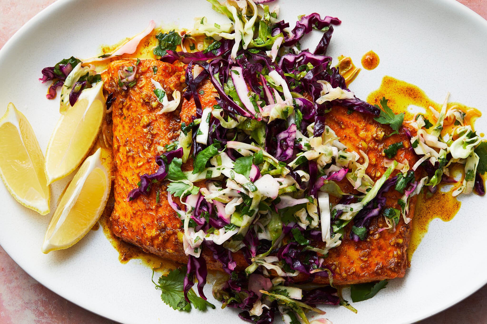 A vibrant orange-spiced salmon fillet topped with a purple and green cabbage slaw and fresh lemon wedges.