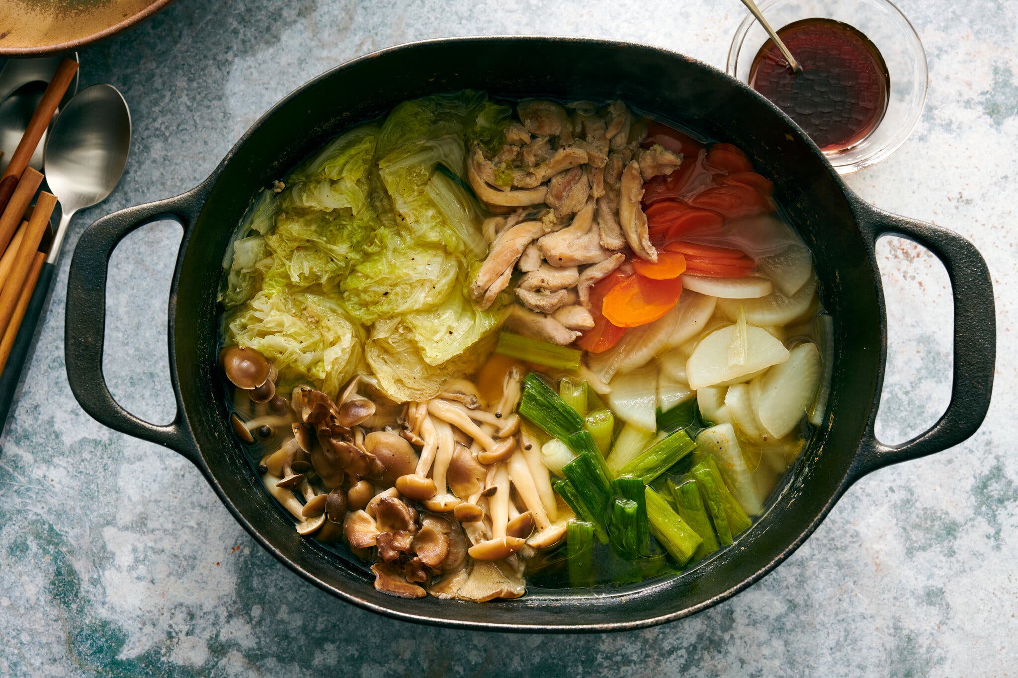 An overhead image of a large cast-iron pot filled with cabbage, chicken, carrots and mushrooms.