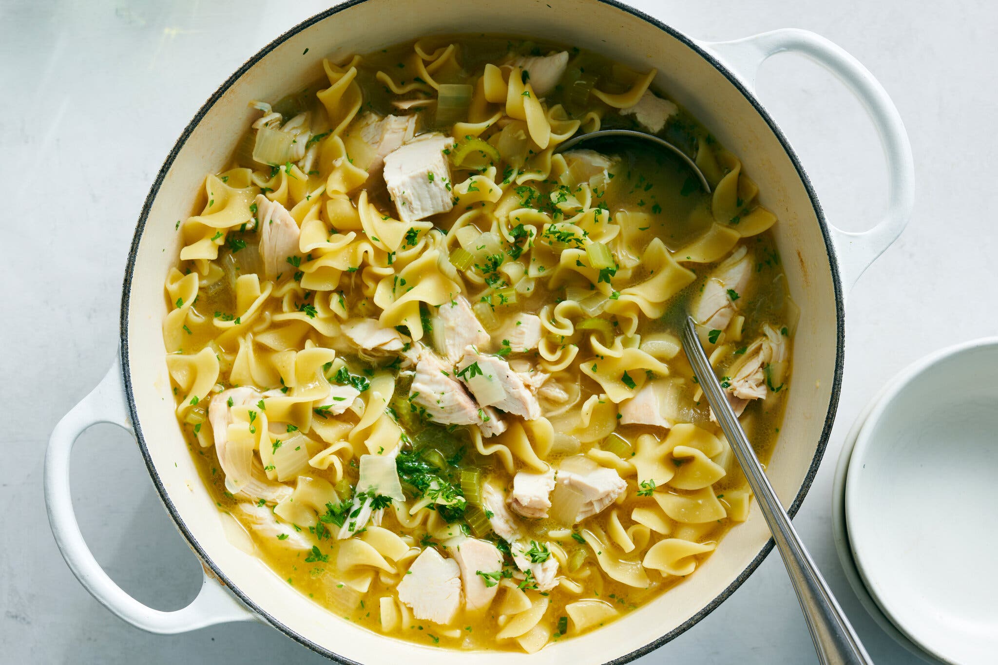 An overhead image of a Dutch oven filled with curly egg noodles and chunks of chicken in a broth.