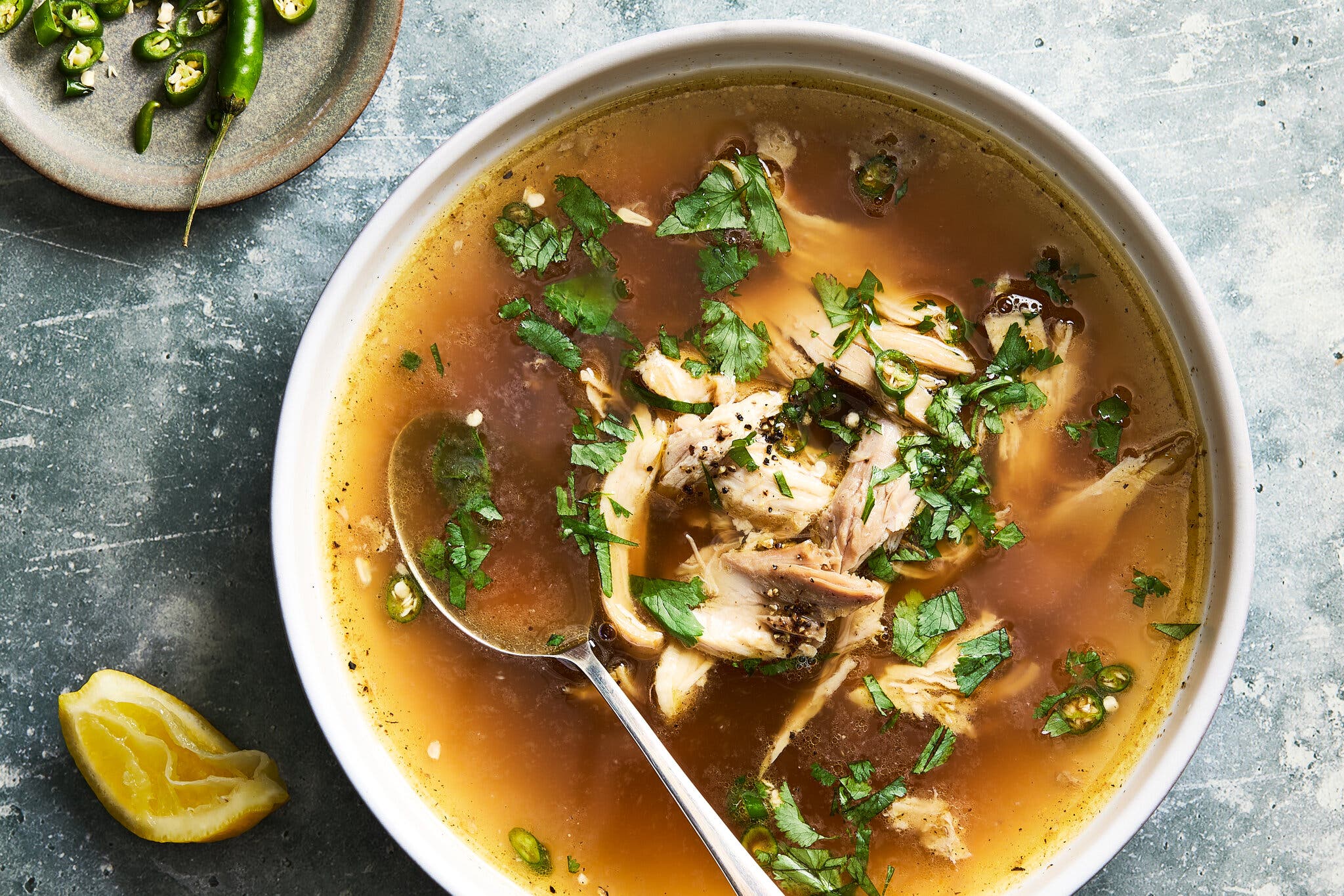 An overhead image of a bowl of chicken soup: shredded chicken in a golden broth scattered with cilantro.
