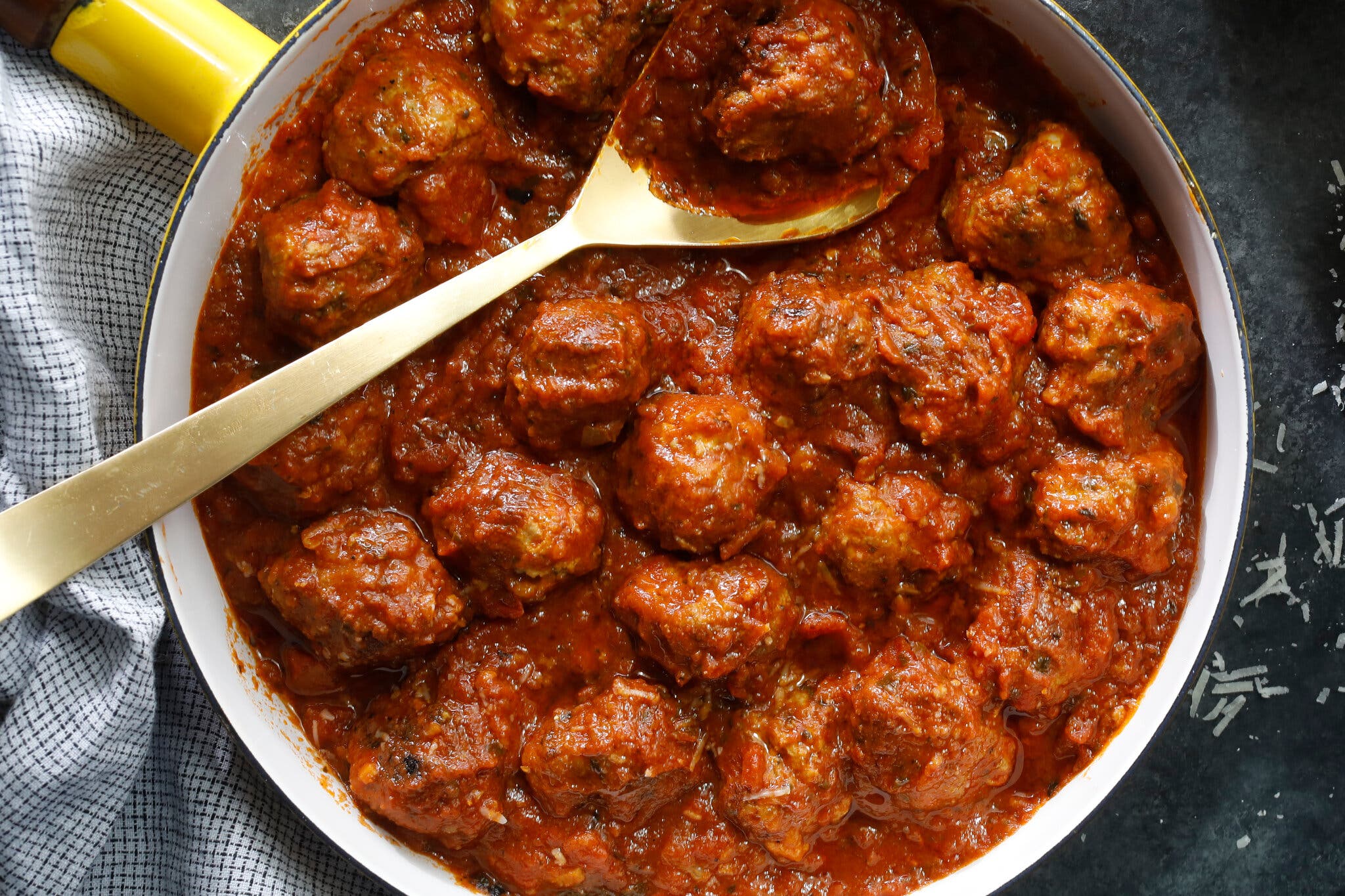An overhead image of a skillet full of turkey meatballs in tomato sauce. There is a golden metal spoon scooping one meatball out of the skillet.