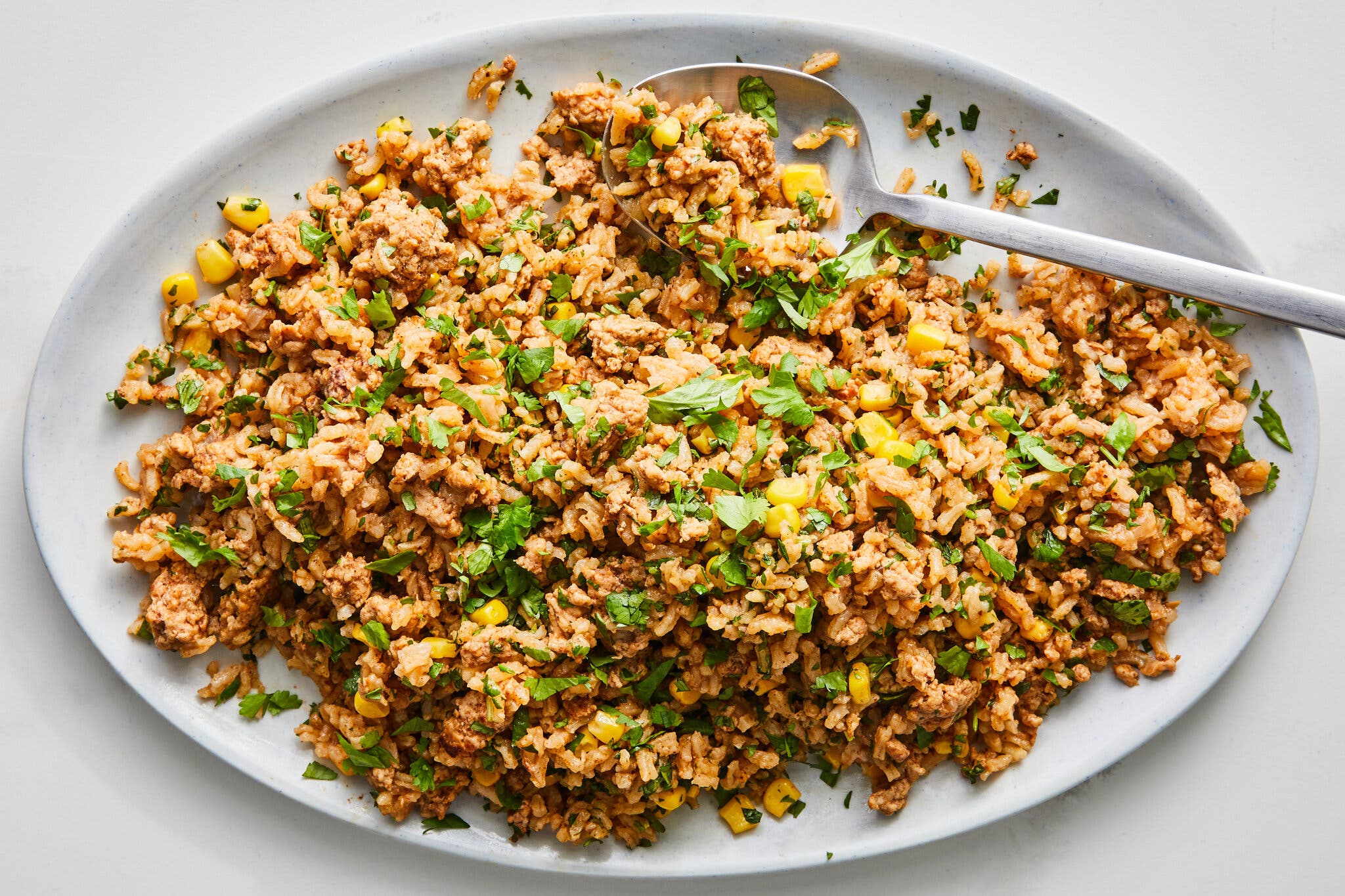 A large platter of turkey and rice with corn kernels, garnished with chopped cilantro.