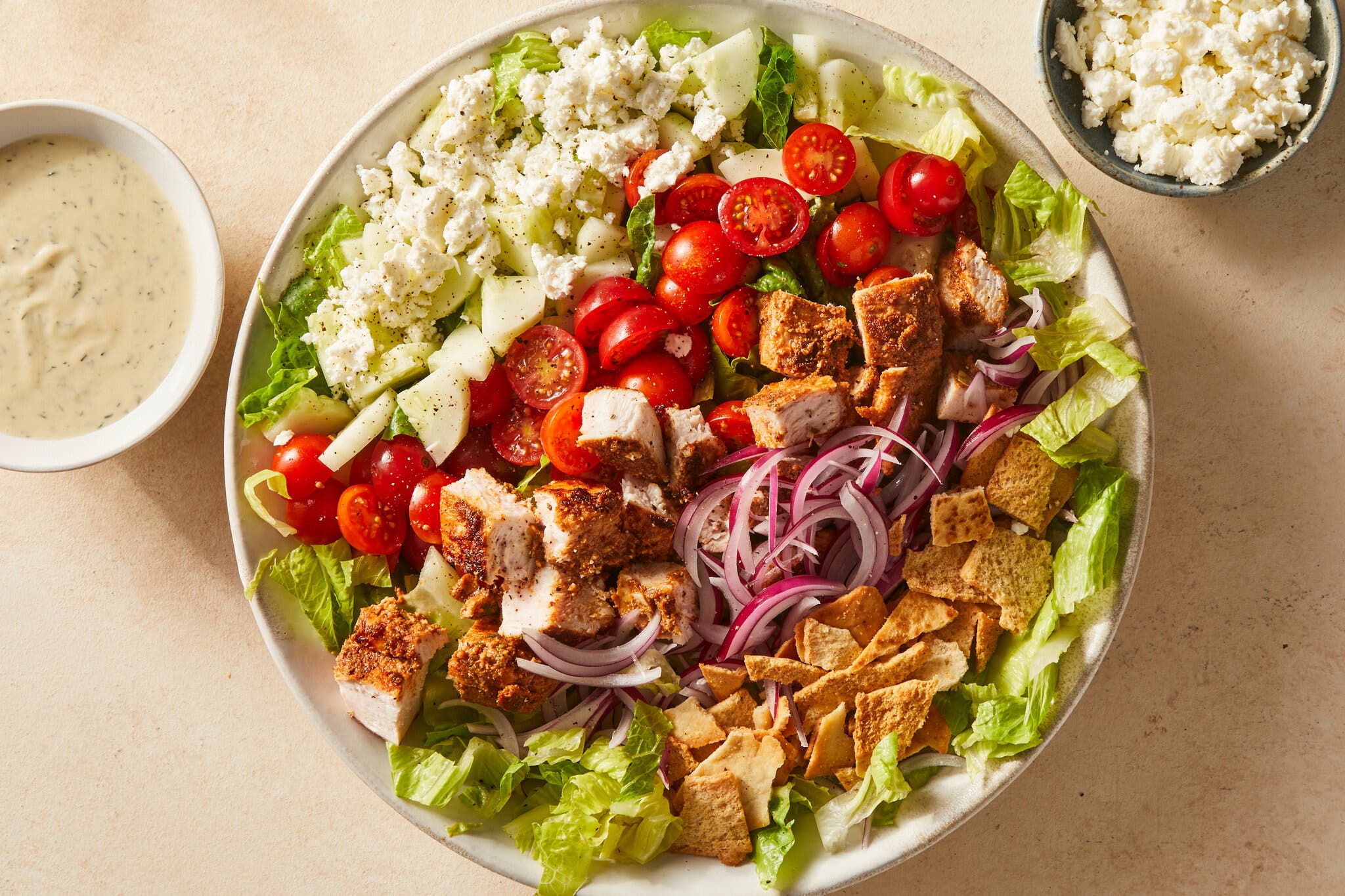 A large salad bowl with grilled chicken, tomatoes, cucumbers, red onion and pita chips.