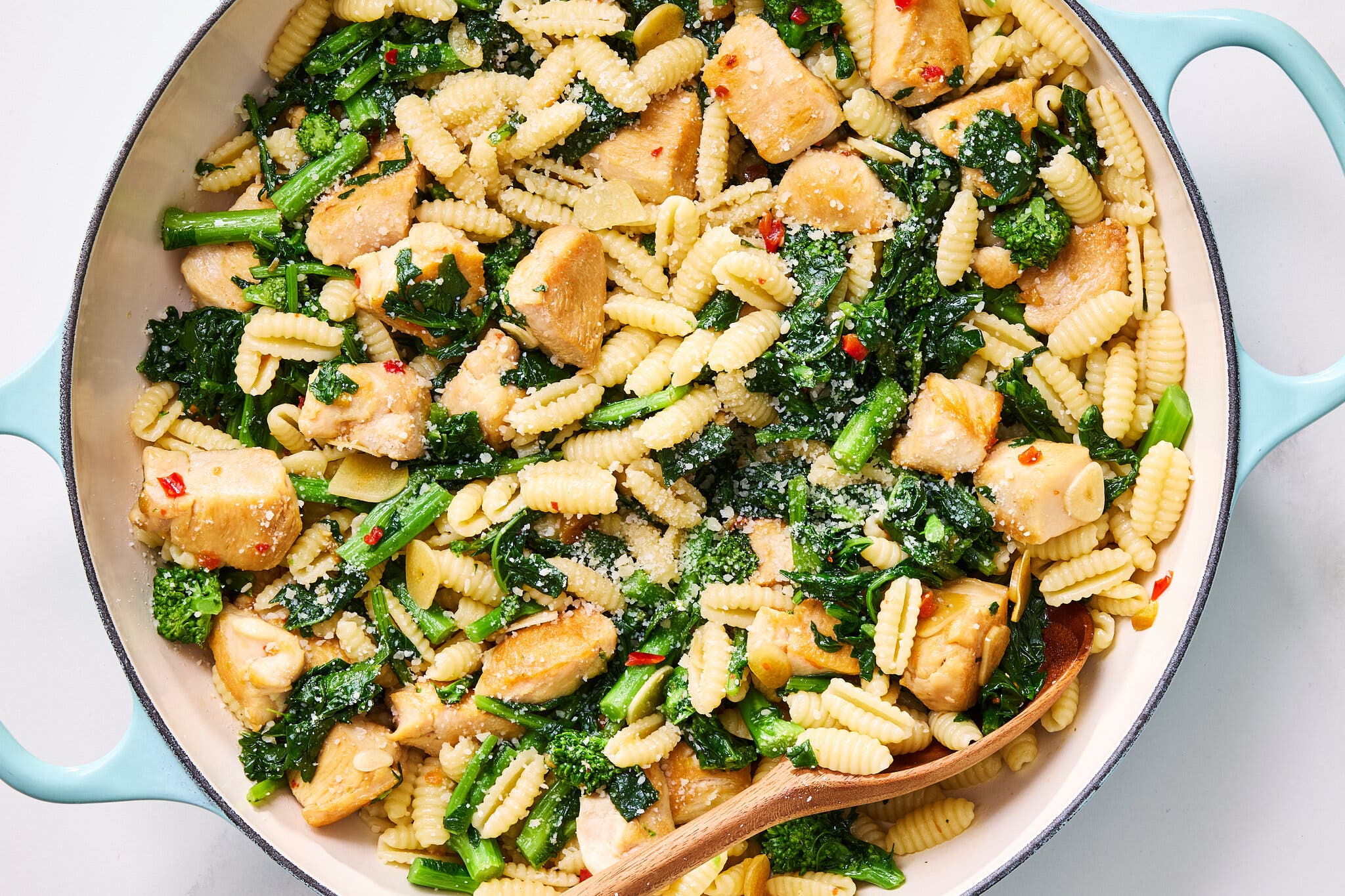 A light blue pan filled with cavatelli pasta, chicken chunks and broccoli rabe.
