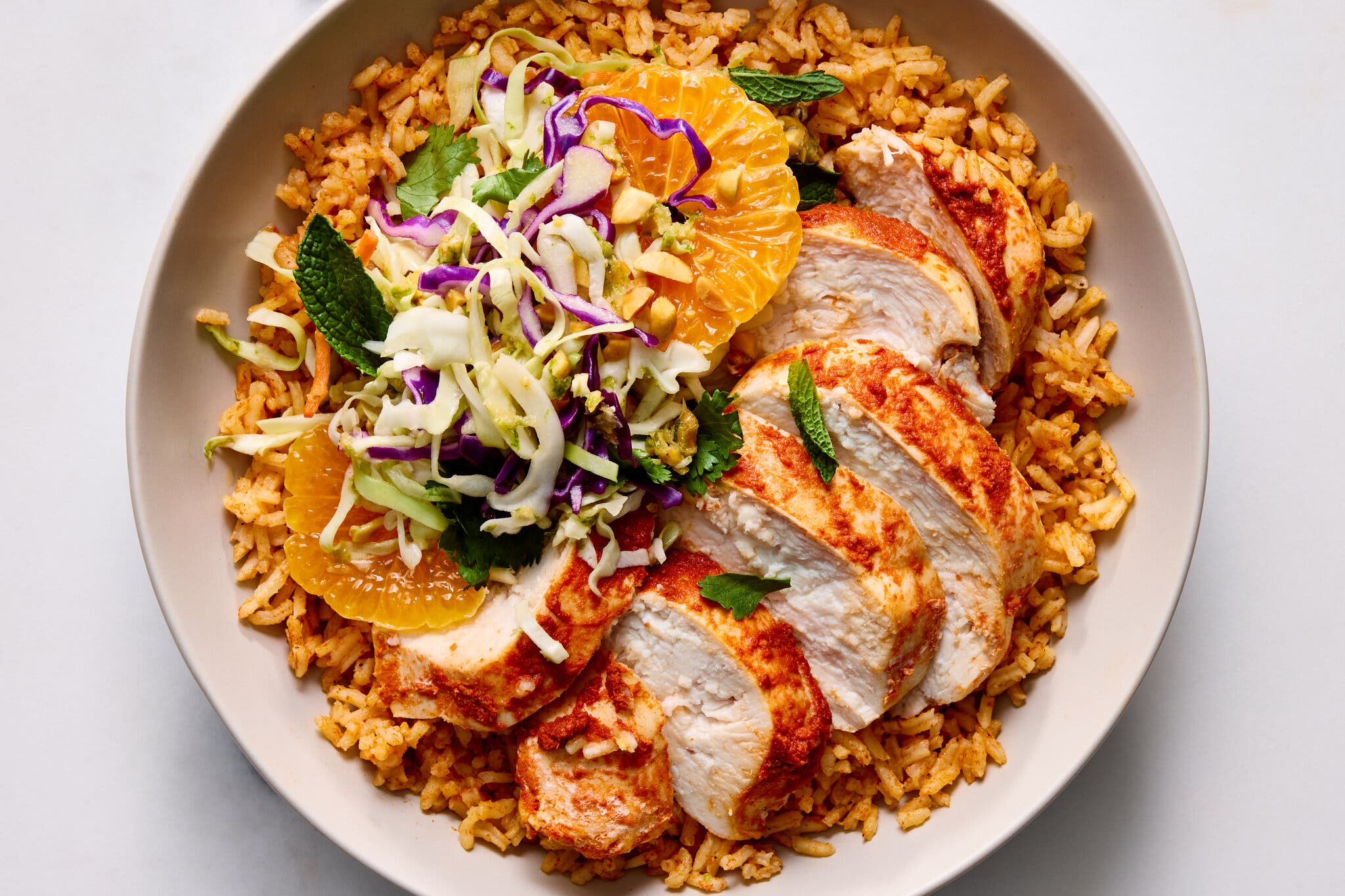 Sliced chicken breast over seasoned rice, topped with a colorful cabbage slaw and bright orange slices.