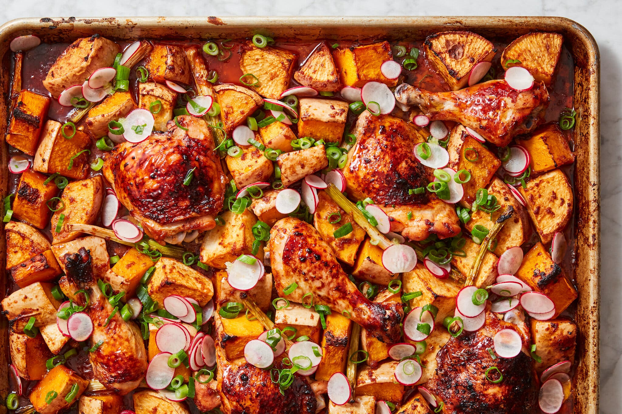 Darkly glazed chicken drumsticks and thighs roasted with cubes of squash and topped with sliced radishes and scallions.