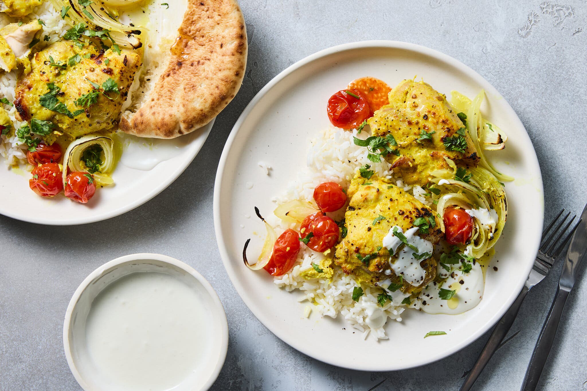 A white plate featuring yellow-seasoned chicken over white rice with roasted tomatoes and onions.