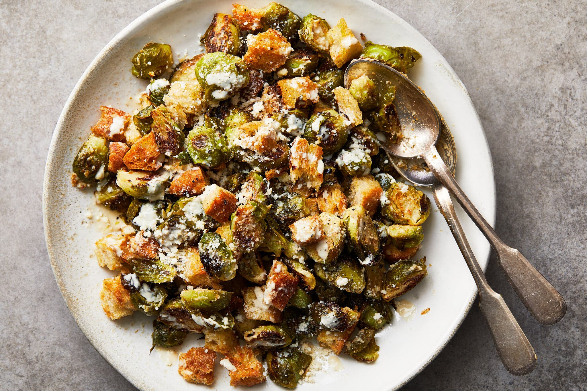 Roasted Brussels sprouts and large golden croutons tossed with white cheese on a light plate.