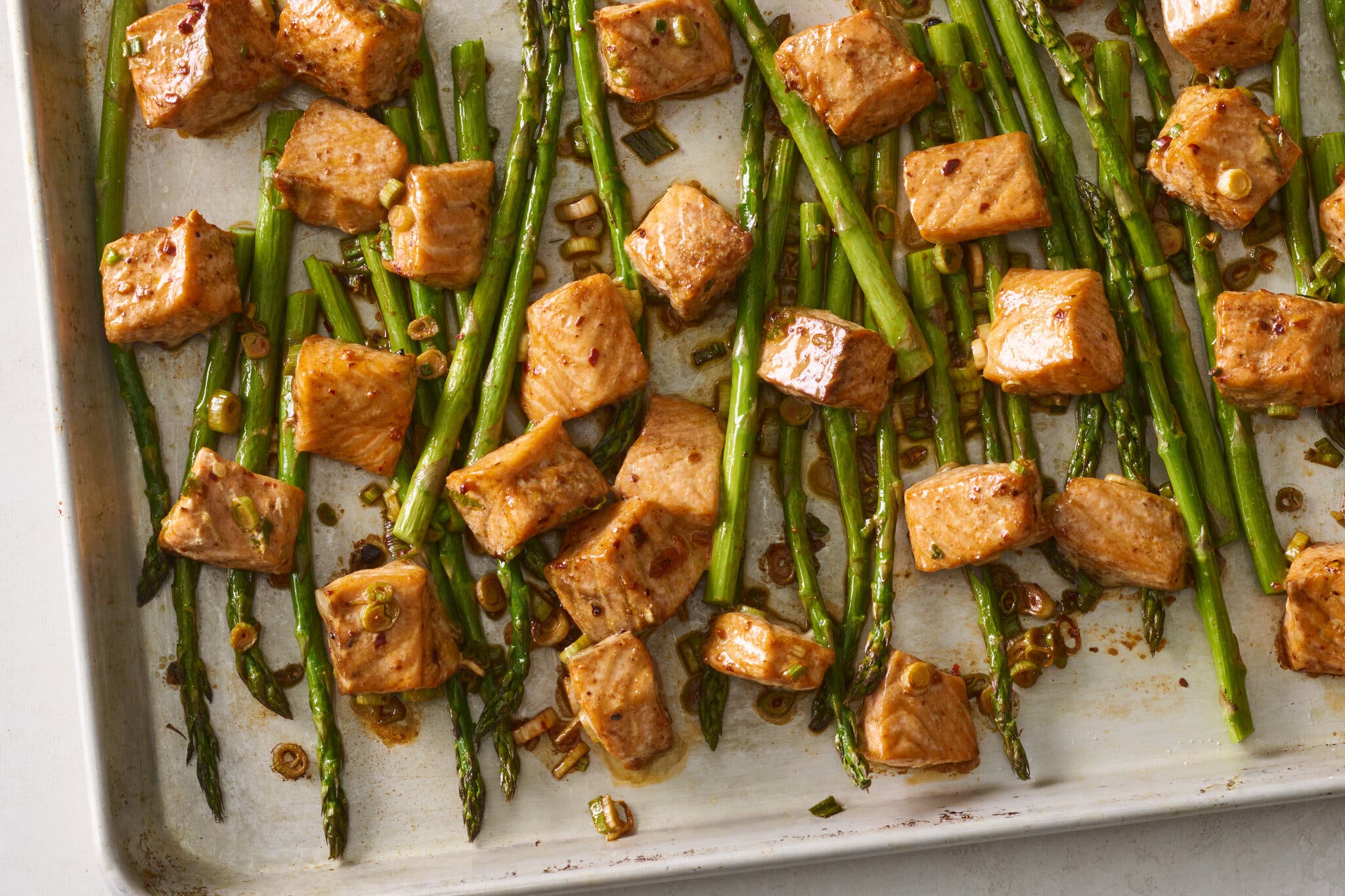 Glazed cubes of salmon and slender green asparagus spears spread across a rimmed baking sheet.