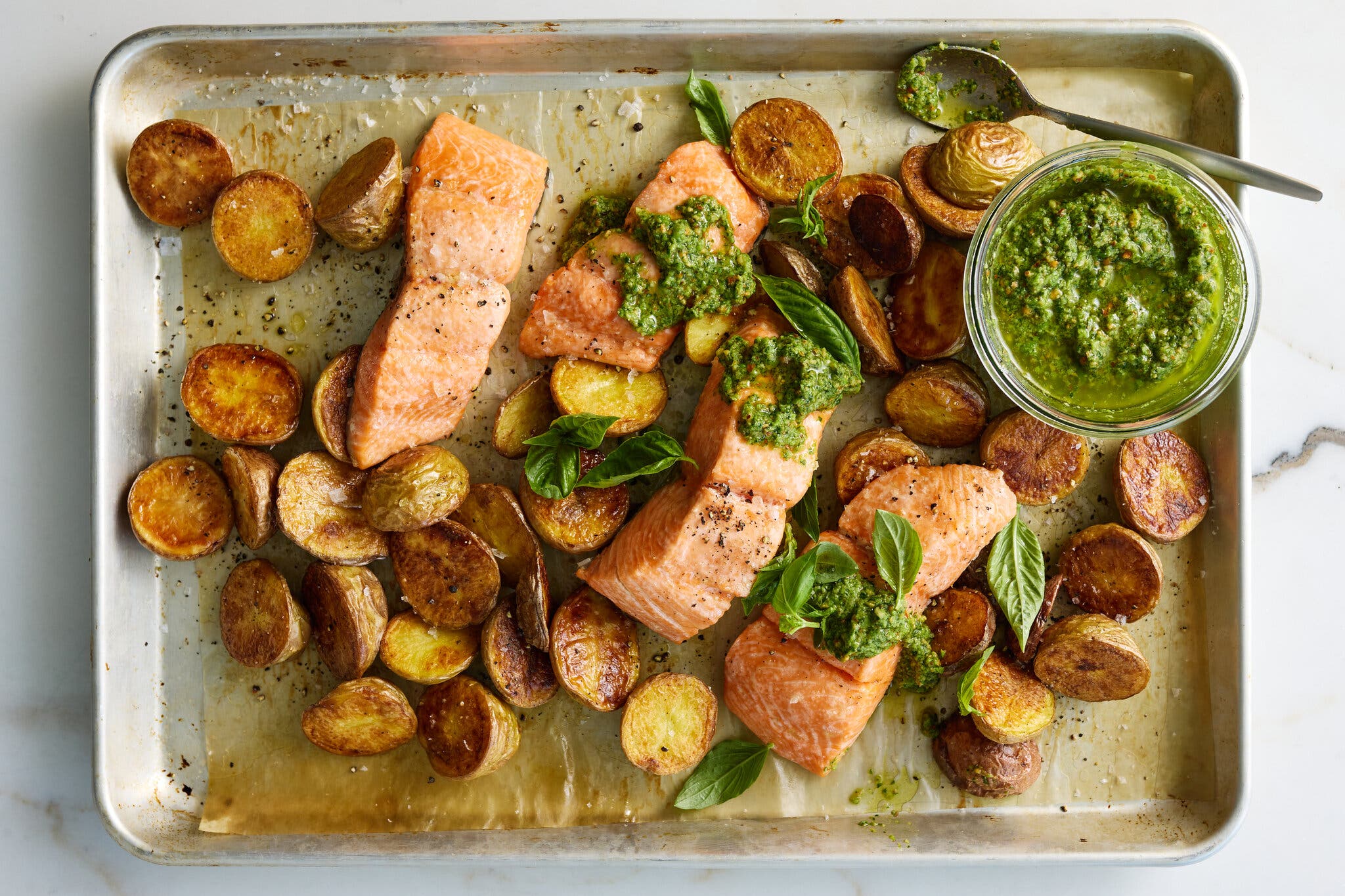 Roasted salmon fillets and crispy halved potatoes on a sheet pan with a side of green pea pesto.