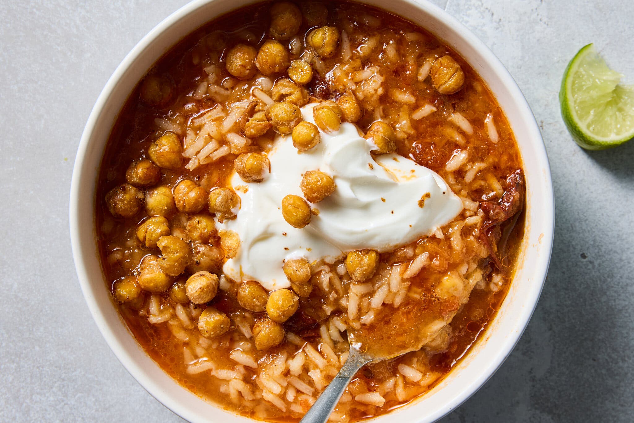 A bowl of tomato-based rice soup topped with crispy chickpeas and a dollop of white cream.