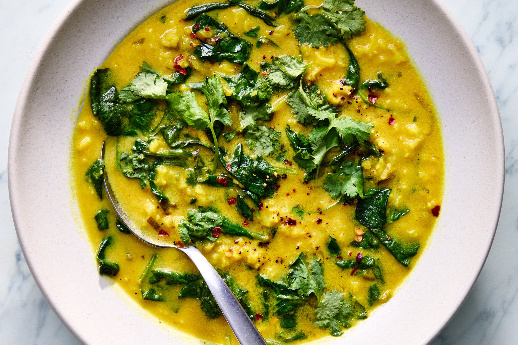 Bright yellow soup topped with wilted spinach, fresh cilantro and red pepper flakes.