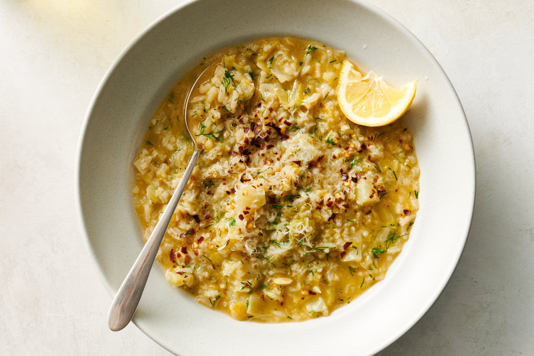 A rustic bowl of rice and cabbage soup topped with black pepper, cheese and a fresh lemon wedge.