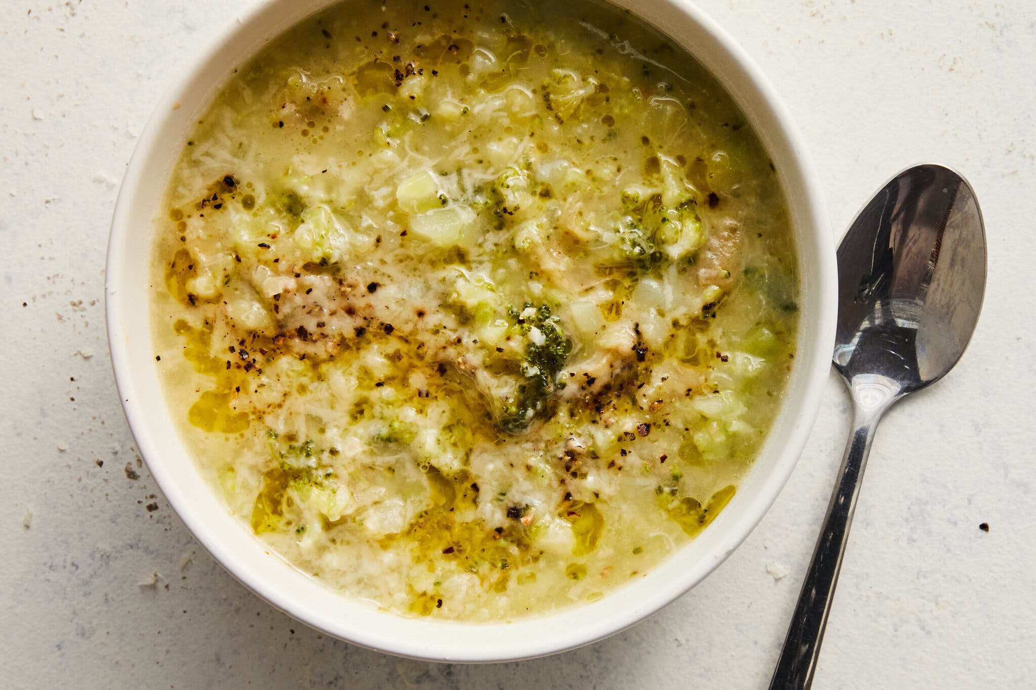 A bowl of thick broccoli and rice soup drizzled with olive oil and sprinkled with black pepper.