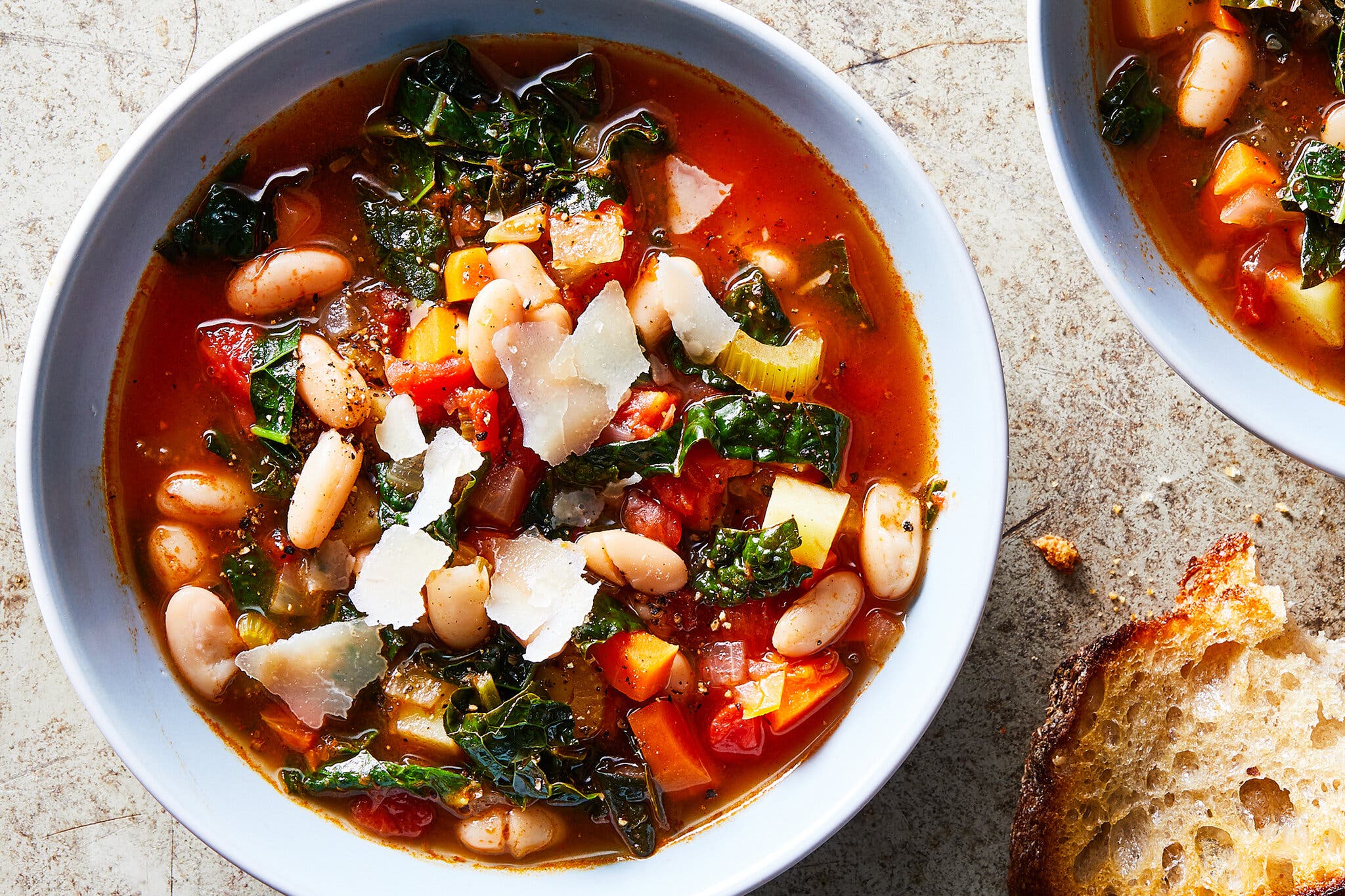 Tomato-based soup with white beans and kale, topped with shaved Parmesan and black pepper.