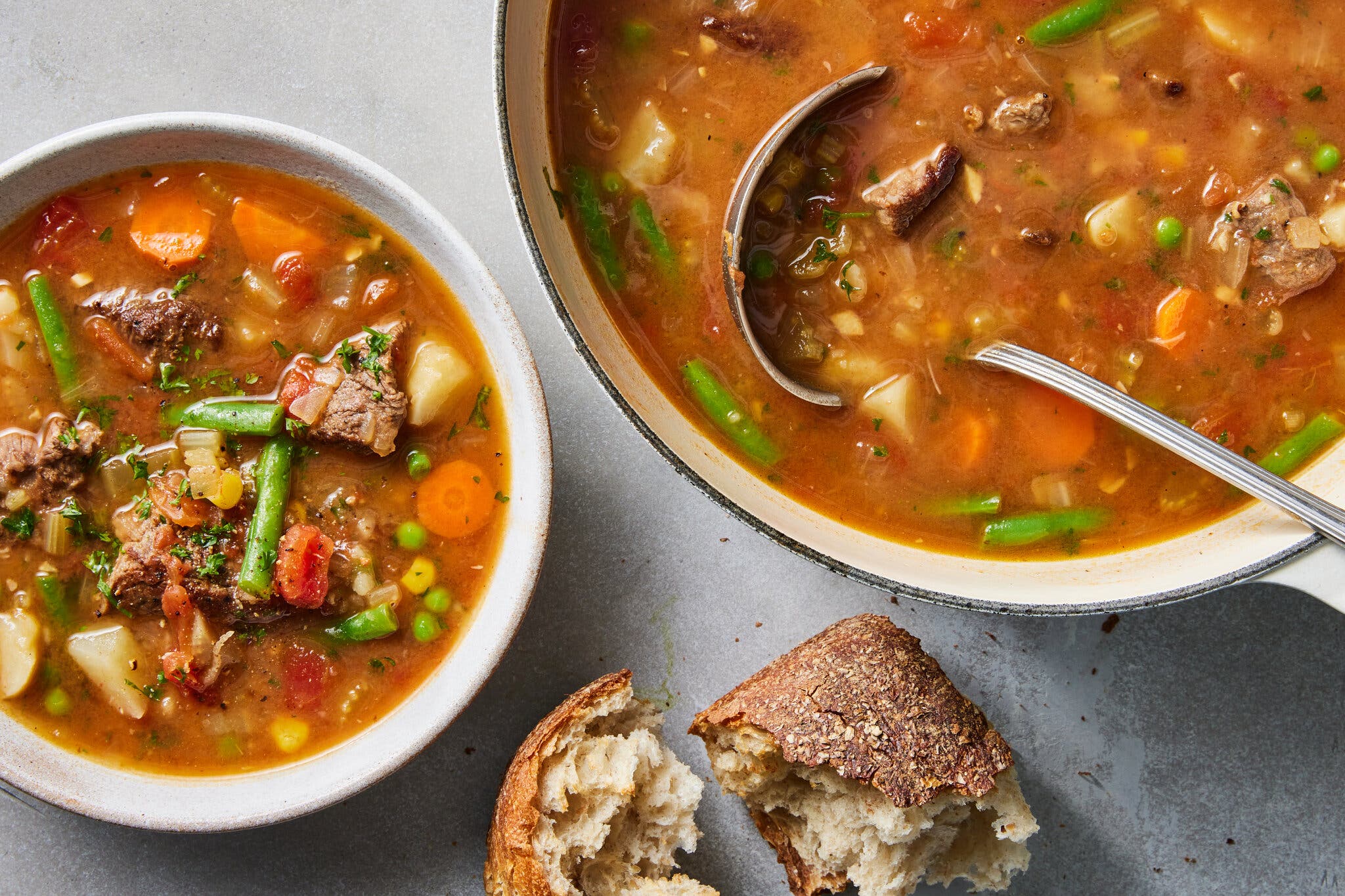 A bowl of chunky beef and vegetable stew served alongside a large piece of crusty, torn bread.