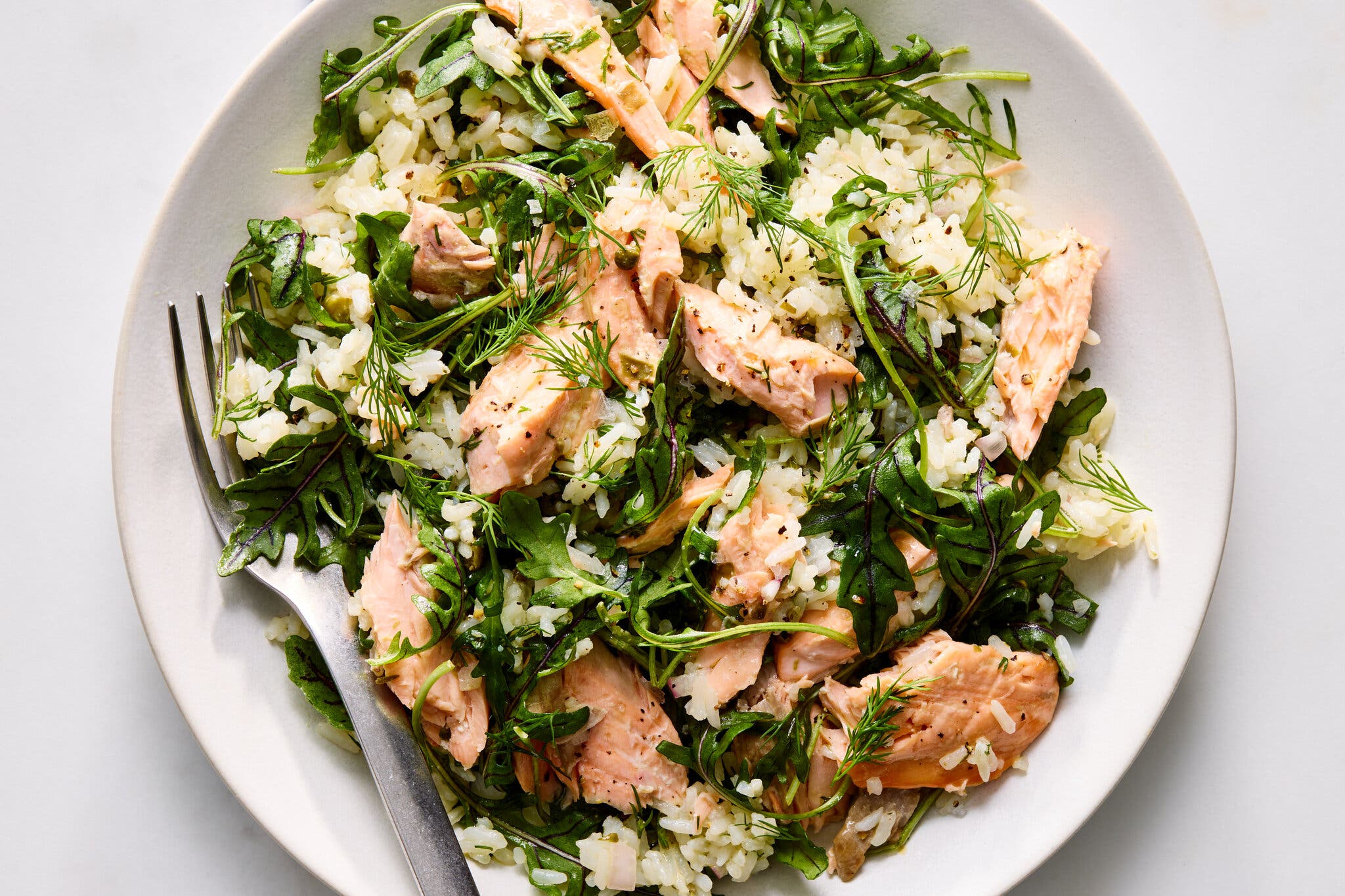 Flaked salmon tossed with white rice, fresh arugula and sprigs of dill on a white plate.
