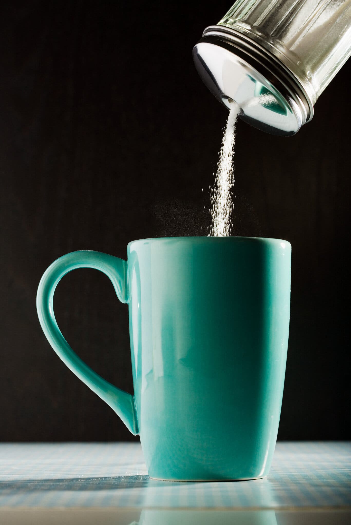 Sugar pours from a dispenser into a green coffee mug.