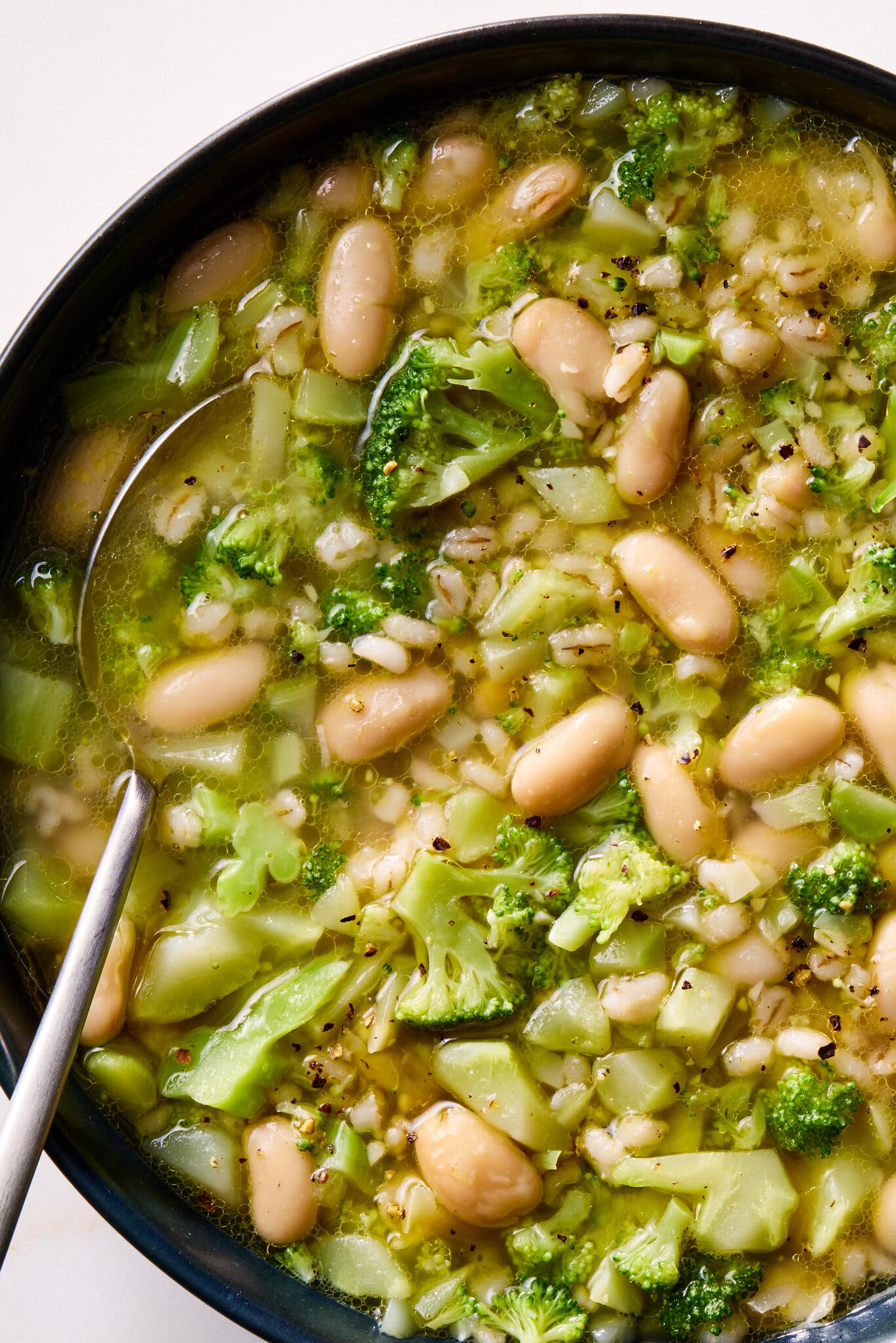 A soup of white beans and broccoli is served in a black bowl.