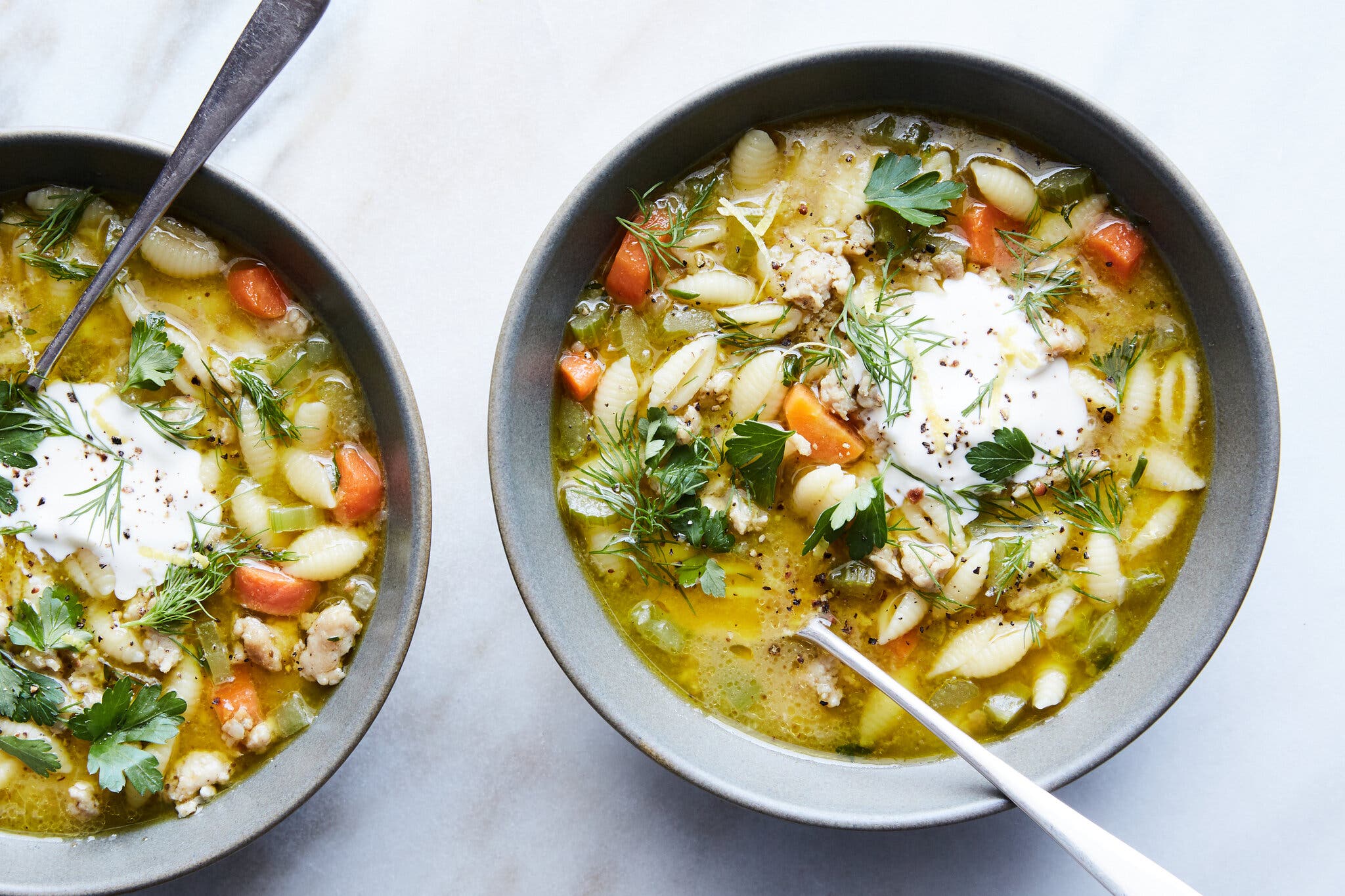 An overhead image of two bowls of chicken soup full of carrots, pasta and chicken.