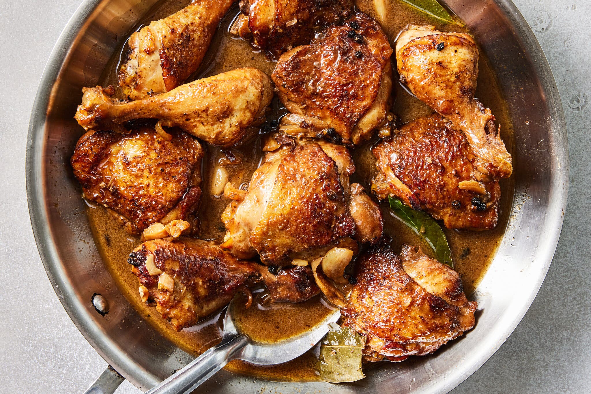 Braised chicken thighs and drumsticks in a dark savory sauce in a stainless steel skillet.