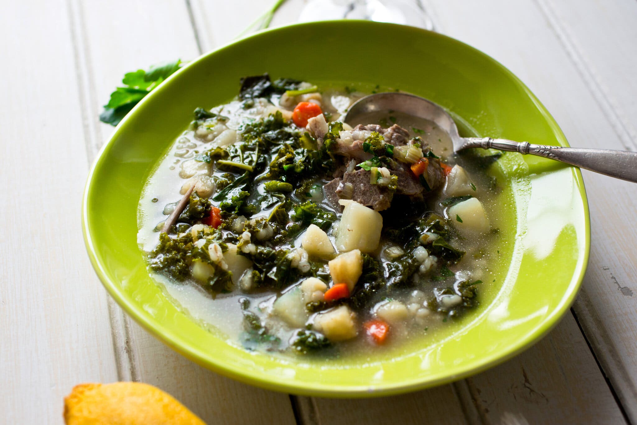 A vibrant green bowl filled with beef, kale and barley soup.