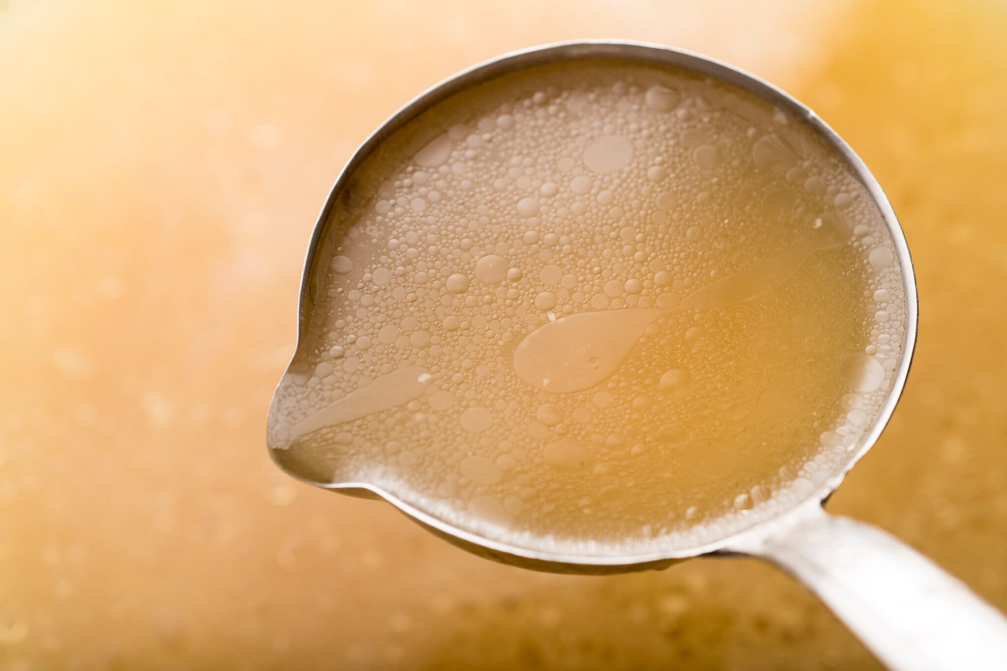 A metal ladle lifting clear, shimmering golden broth.