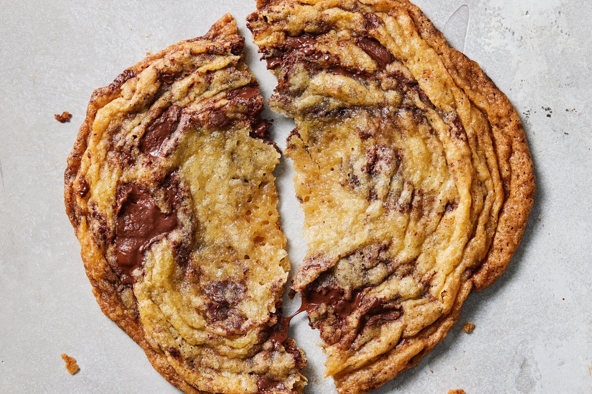 A large, chewy chocolate chip cookie pulled apart into two jagged halves with melted chocolate.