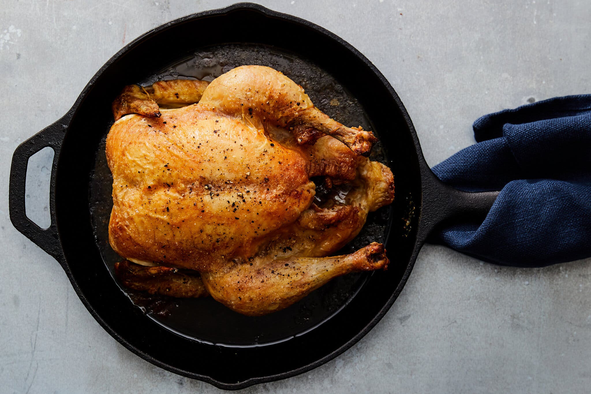 A whole roasted chicken with crispy, seasoned skin served in a black cast-iron skillet.