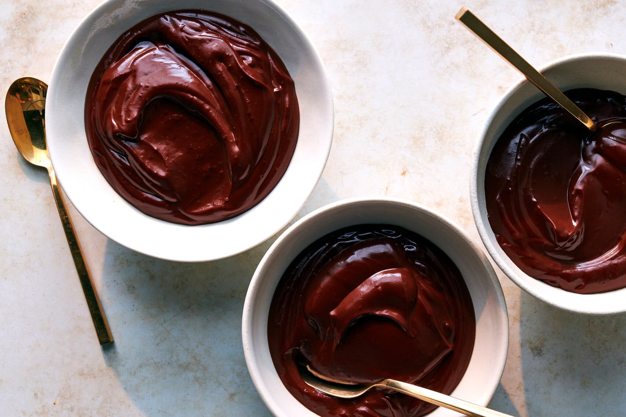 An overhead image of bowls of dark, glossy chocolate pudding. There are spoons in two of the bowls.