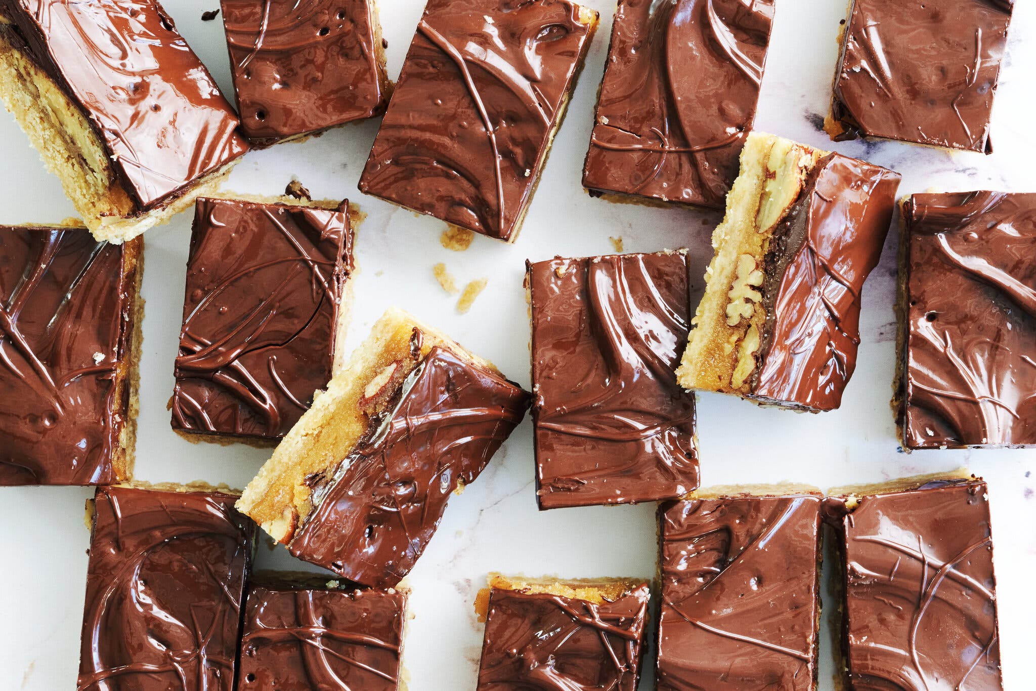 Turtle bars, with a layer of chocolate, caramel, nuts and shortbread, seen cross-sectioned from overhead, on a marble countertop.
