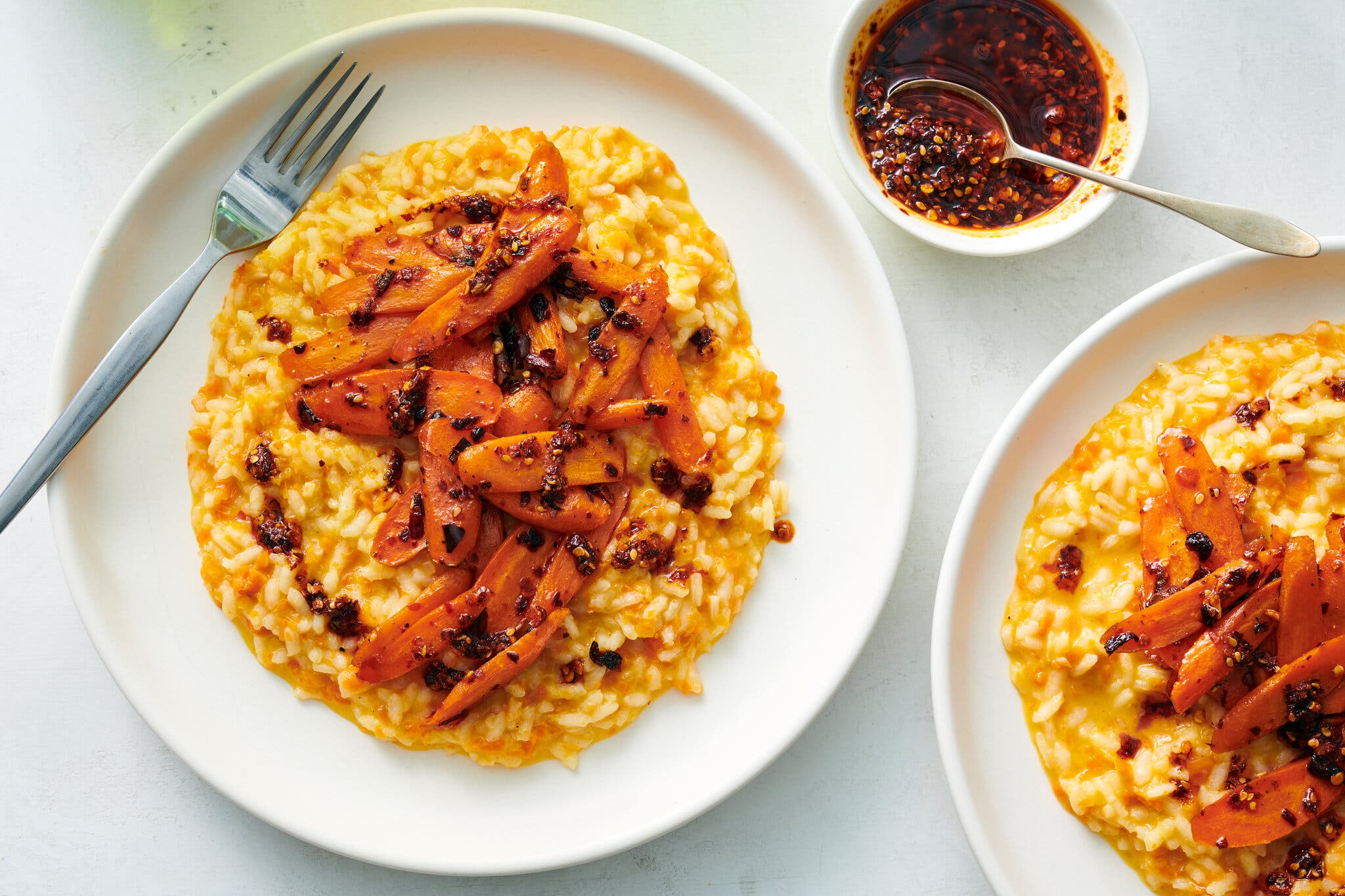 Creamy orange risotto topped with sliced roasted carrots and a dark chili oil drizzle.
