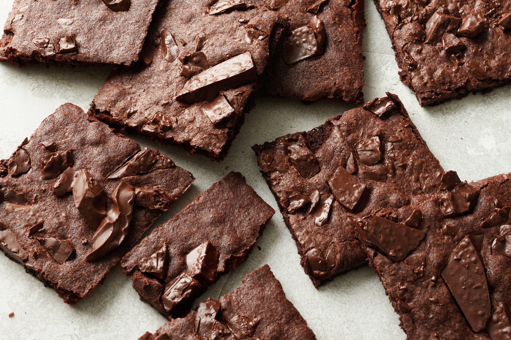An image of thin brownie bark, studded with pieces of chocolate, on a flat surface