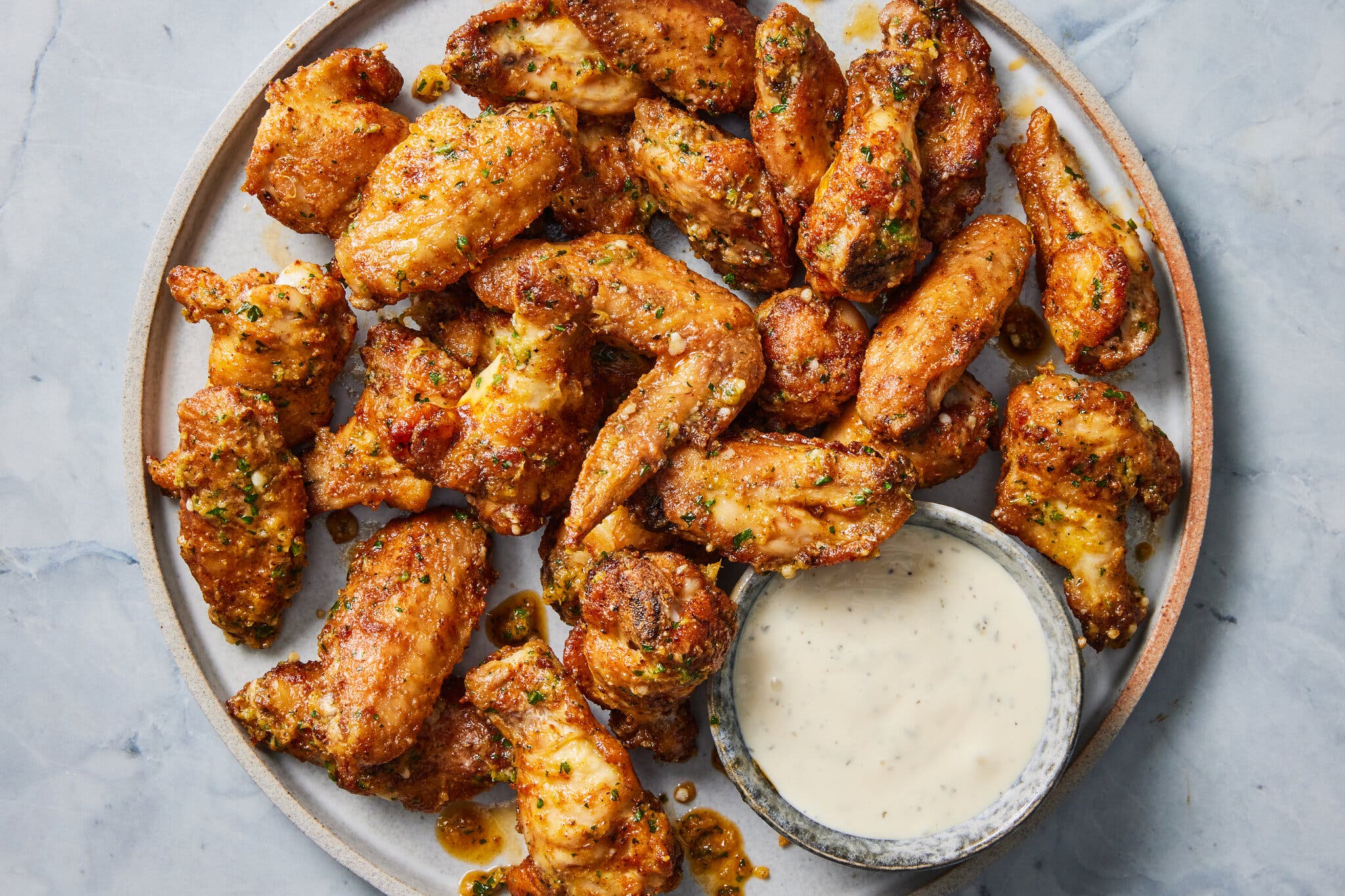 An overhead image of chicken wings on a plate next to a small dipping sauce.
